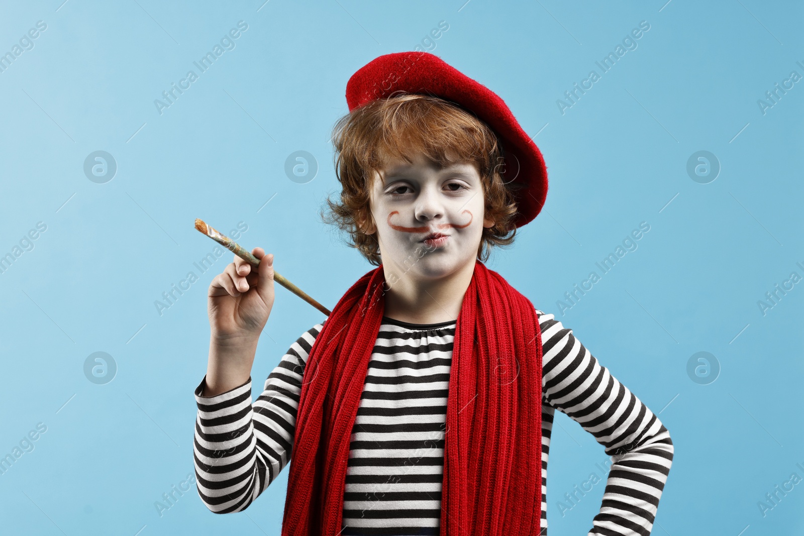 Photo of Cute boy in mime costume with brush on light blue background. Surprise party