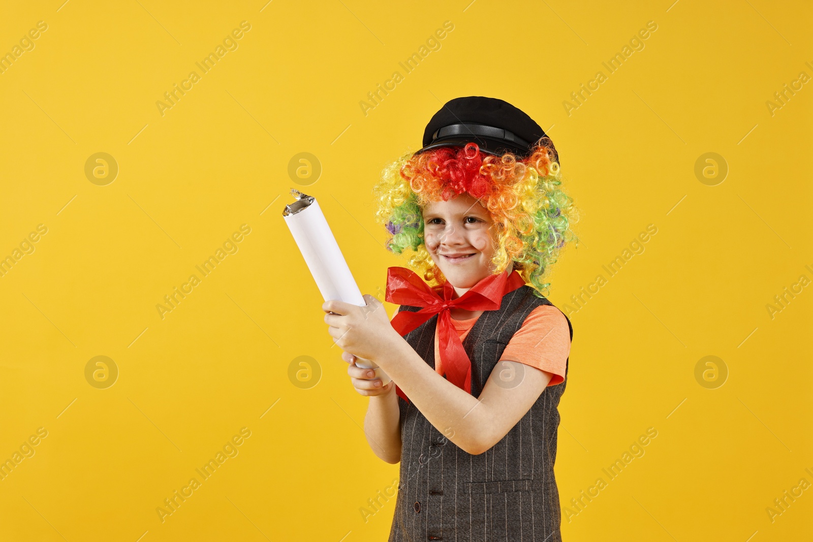 Photo of Happy little boy dressed like clown with confetti popper on yellow background. Surprise party