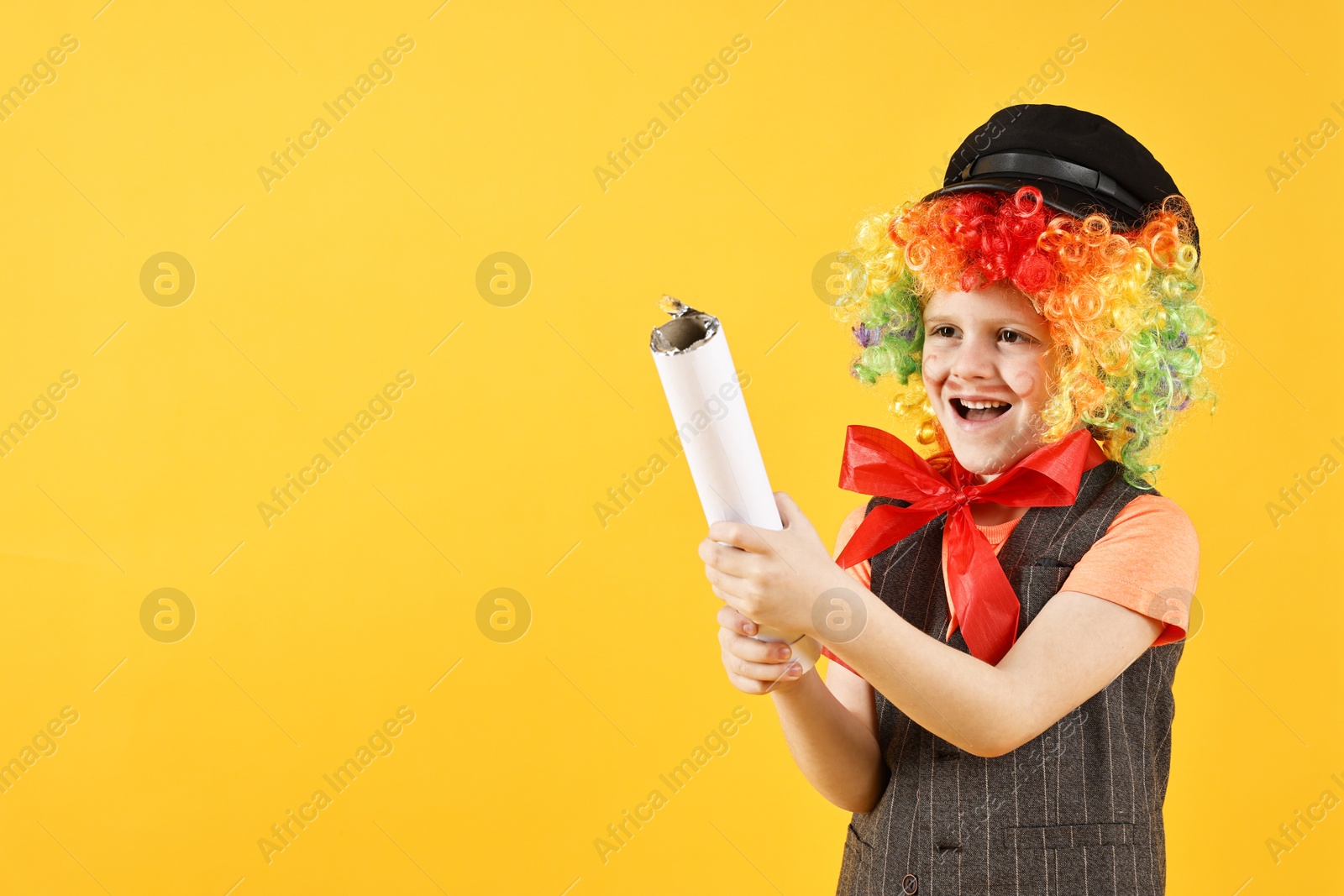 Photo of Happy little boy dressed like clown with confetti popper on yellow background, space for text. Surprise party