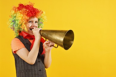 Photo of Happy boy in clown wig with megaphone on yellow background, space for text. Surprise party