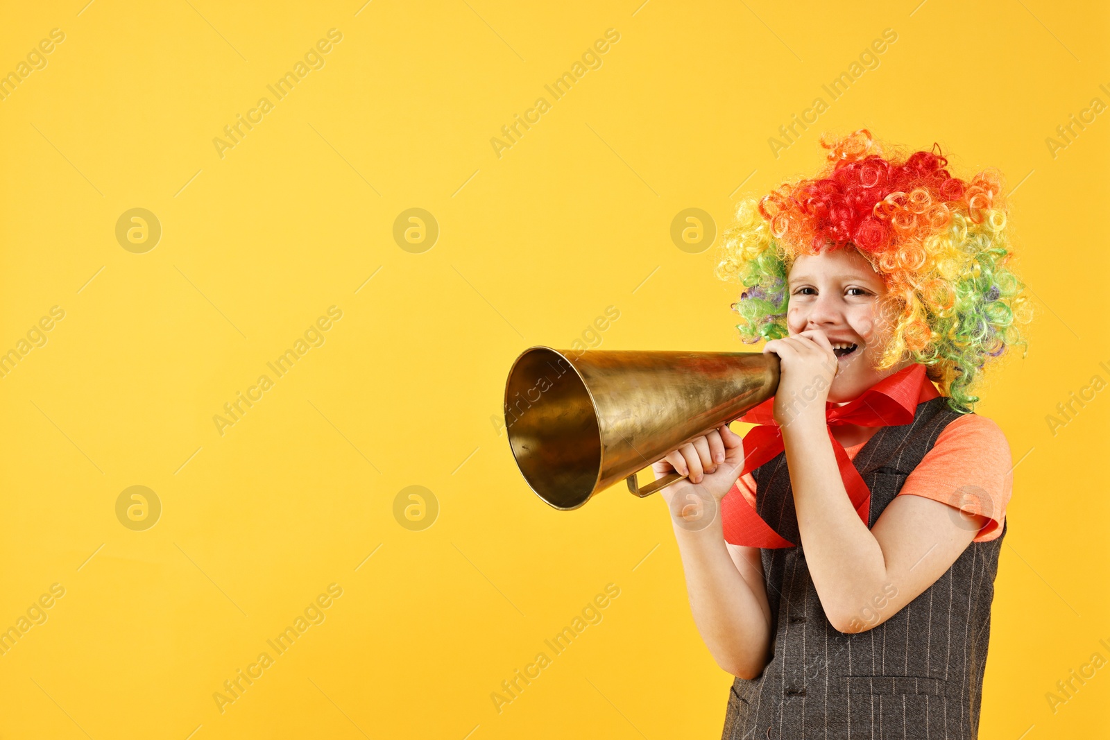 Photo of Happy boy in clown wig with megaphone on yellow background, space for text. Surprise party