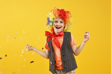 Photo of Happy little boy dressed like clown and flying confetti on orange background. Surprise party