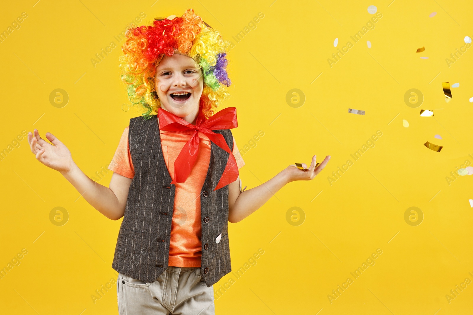 Photo of Happy little boy dressed like clown and flying confetti on orange background. Surprise party