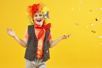 Happy little boy dressed like clown and flying confetti on orange background. Surprise party