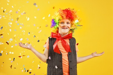 Photo of Happy little boy dressed like clown and flying confetti on orange background. Surprise party