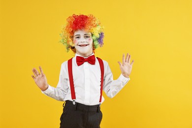 Photo of Happy little boy dressed like clown on yellow background, space for text. Surprise party