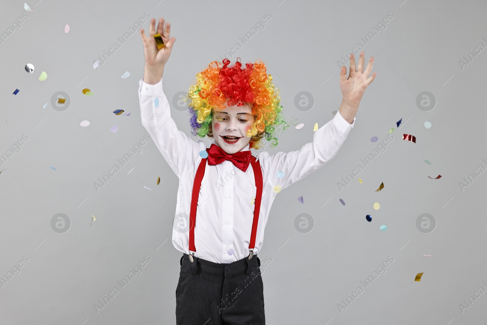 Photo of Happy little boy dressed like clown and flying confetti on grey background. Surprise party