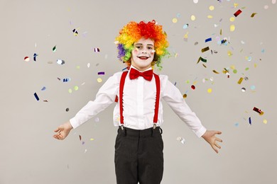 Photo of Happy little boy dressed like clown and flying confetti on grey background. Surprise party