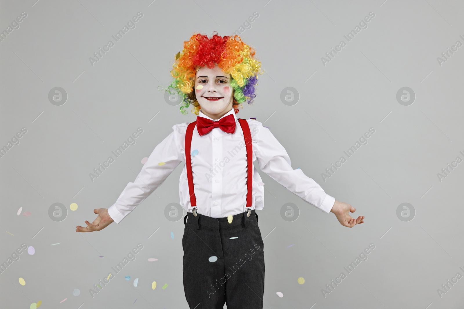 Photo of Happy little boy dressed like clown and flying confetti on grey background. Surprise party