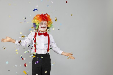 Photo of Happy little boy dressed like clown and flying confetti on grey background, space for text. Surprise party