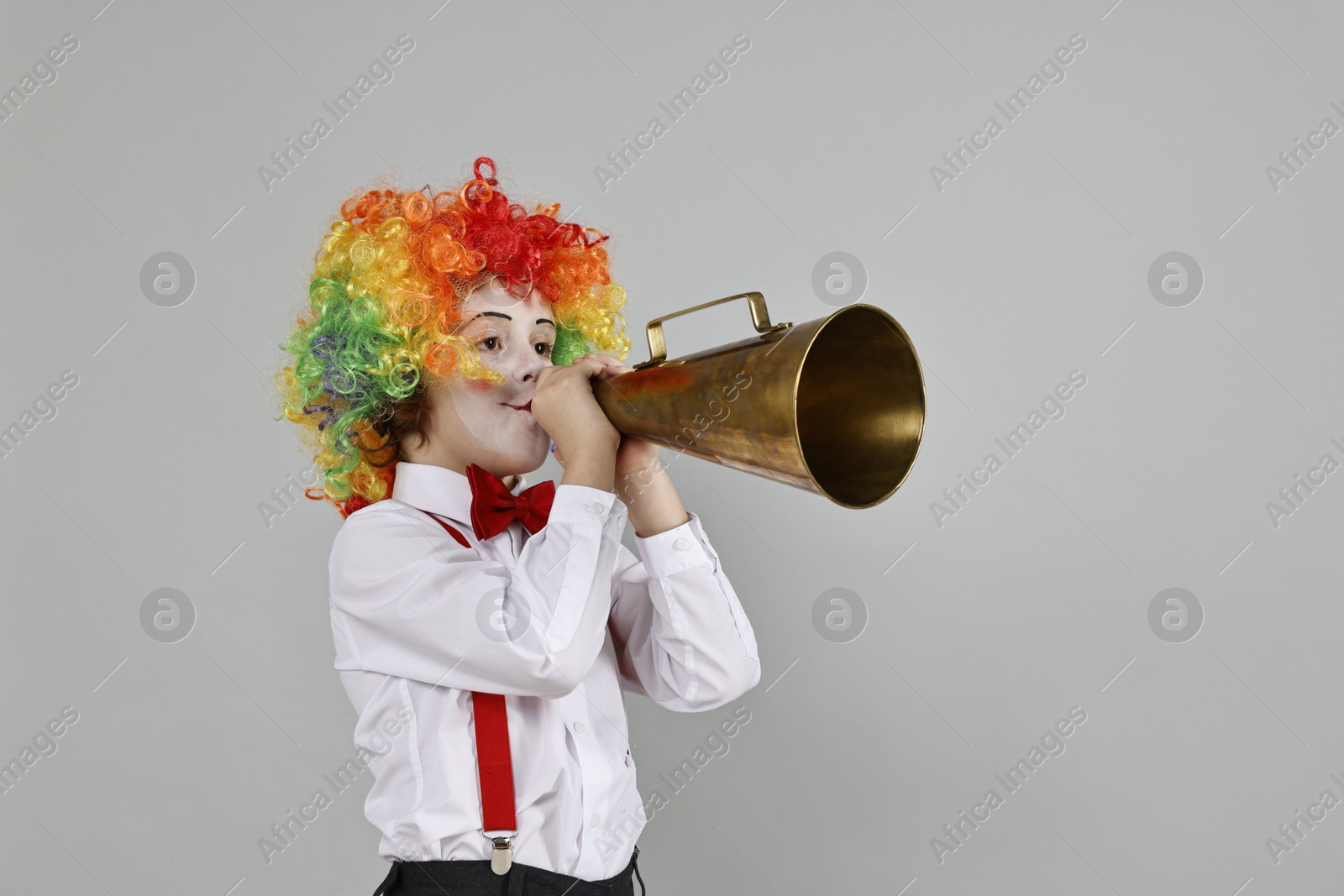 Photo of Little boy dressed like clown with megaphone on grey background, space for text. Surprise party