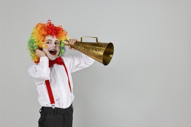 Photo of Little boy dressed like clown with megaphone on grey background, space for text. Surprise party