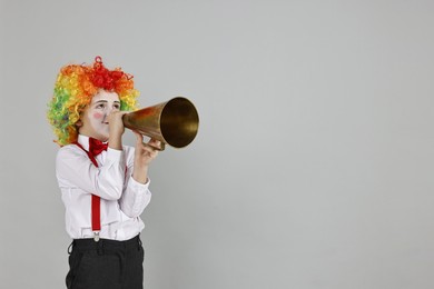 Photo of Little boy dressed like clown with megaphone on grey background, space for text. Surprise party