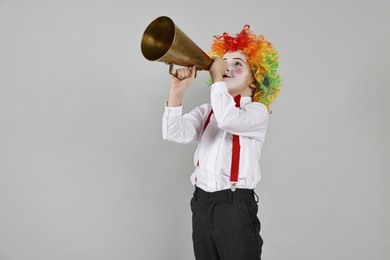 Photo of Little boy dressed like clown with megaphone on grey background, space for text. Surprise party