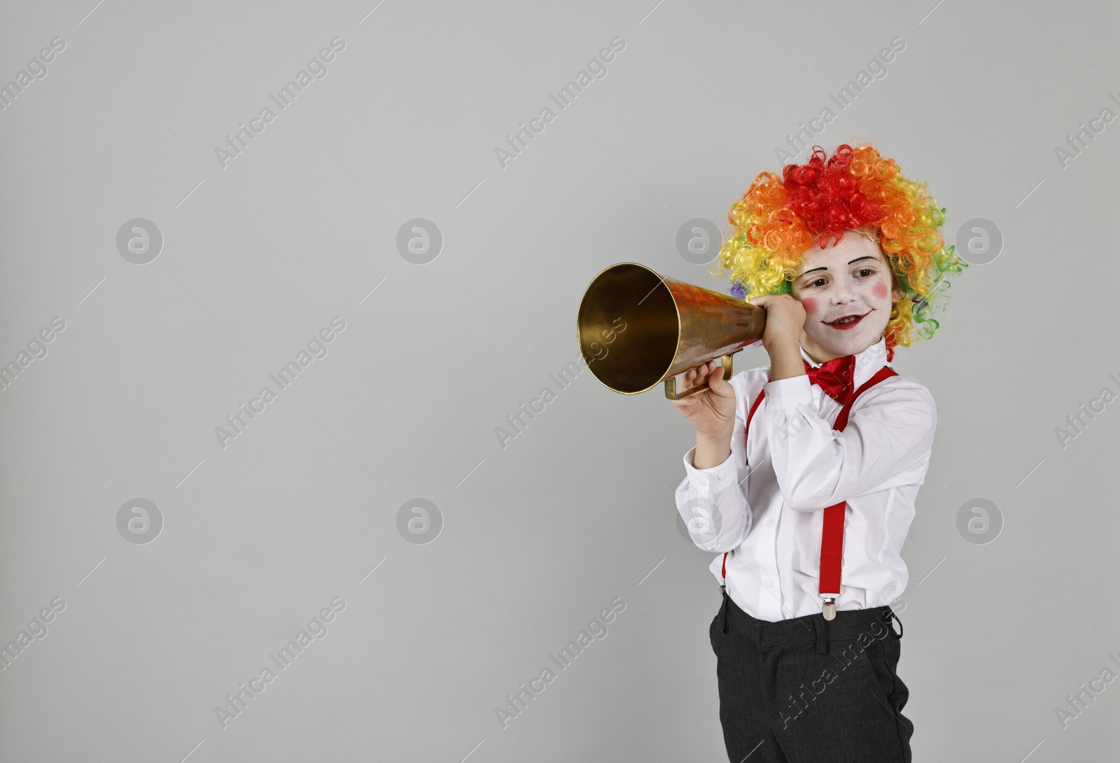 Photo of Happy little boy dressed like clown with megaphone on grey background, space for text. Surprise party