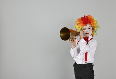 Happy little boy dressed like clown with megaphone on grey background, space for text. Surprise party