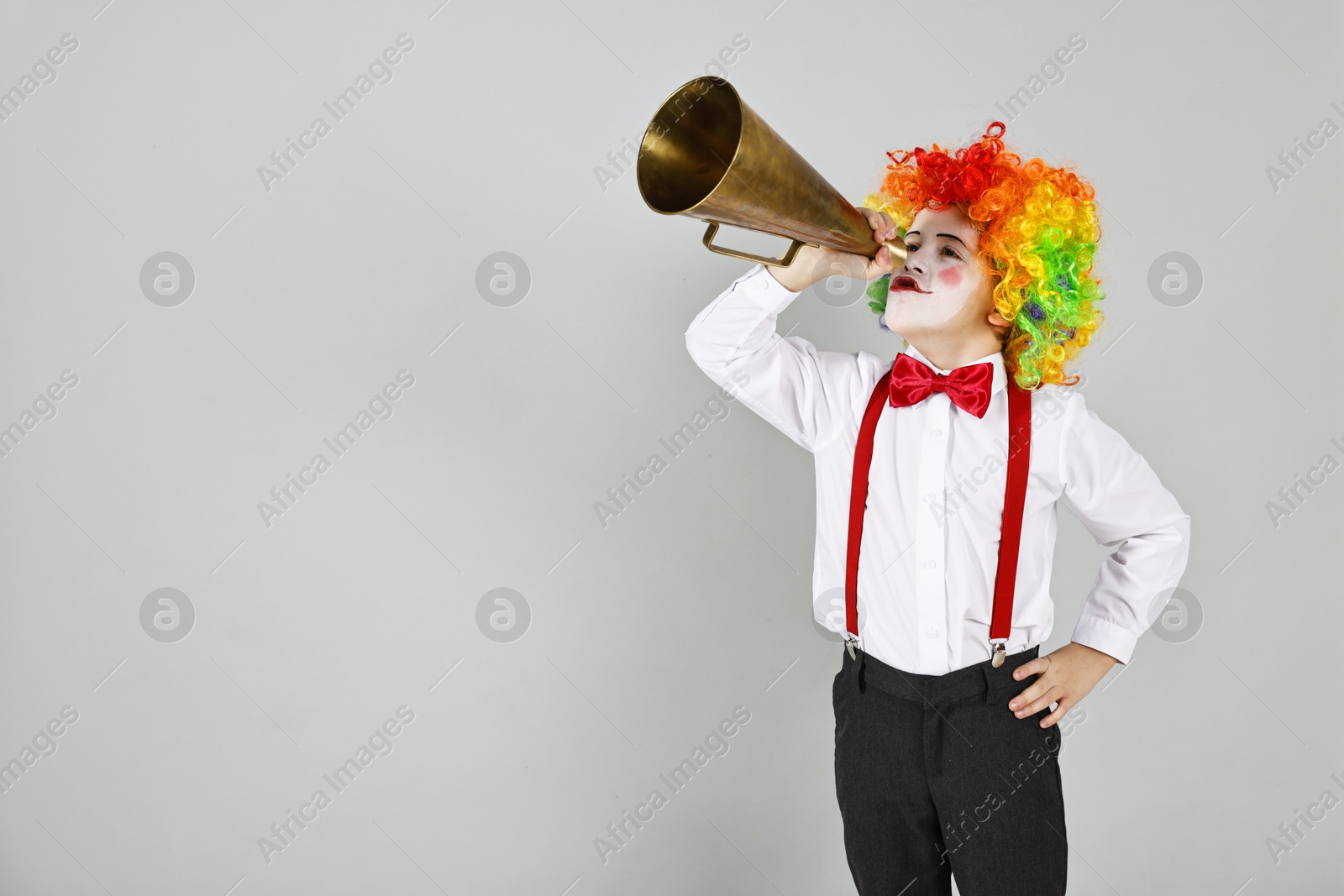 Photo of Little boy dressed like clown with megaphone on grey background, space for text. Surprise party