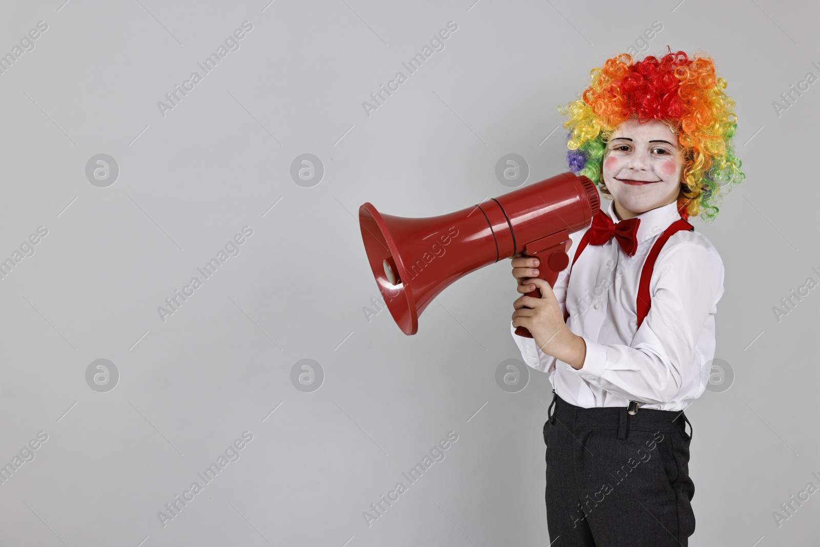 Photo of Little boy dressed like clown with megaphone on grey background, space for text. Surprise party