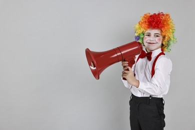 Photo of Little boy dressed like clown with megaphone on grey background, space for text. Surprise party