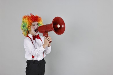 Photo of Little boy dressed like clown shouting in megaphone on grey background, space for text. Surprise party