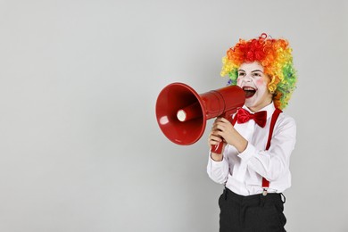 Little boy dressed like clown shouting in megaphone on grey background, space for text. Surprise party