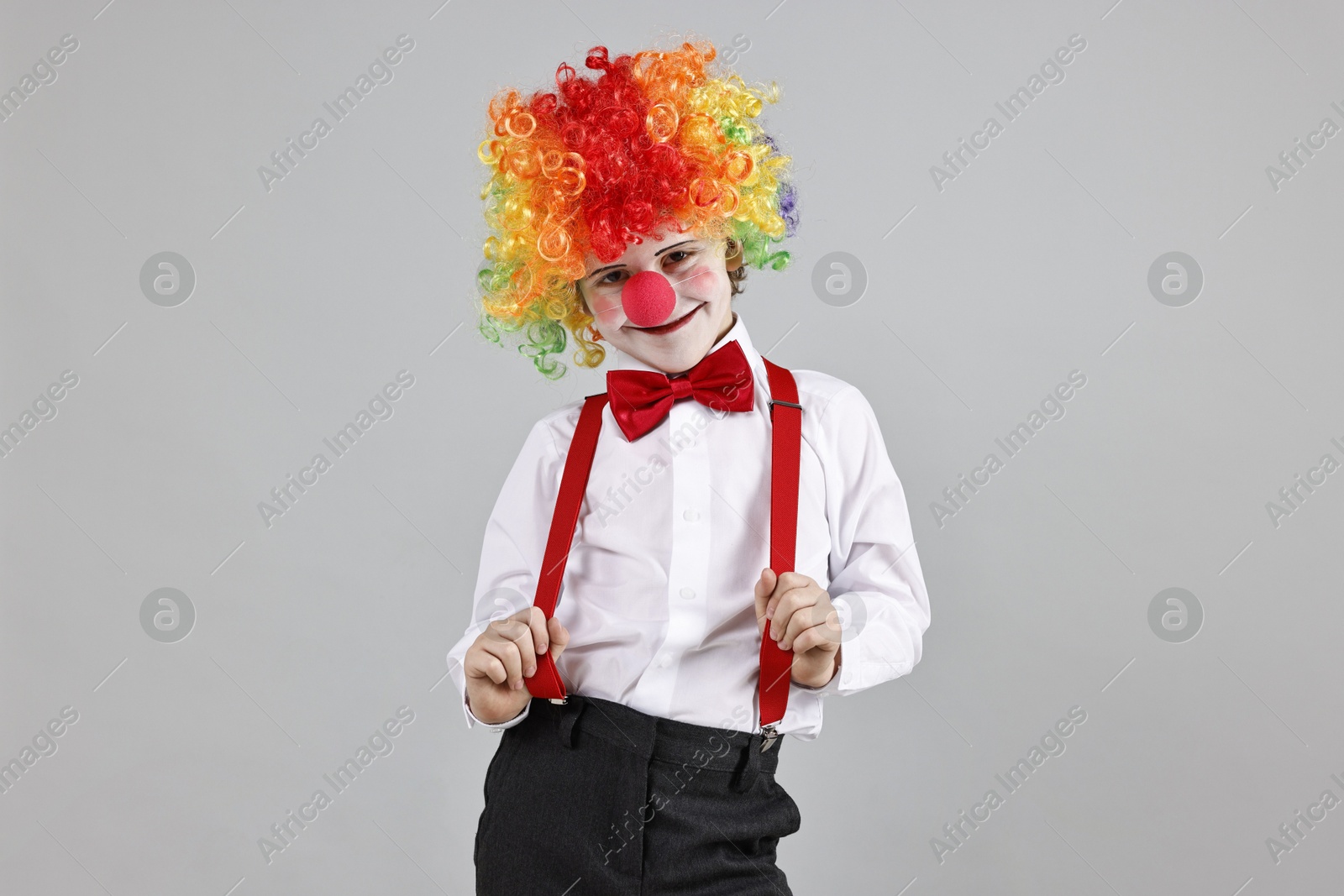 Photo of Cute little boy in clown wig and red nose on grey background. Surprise party