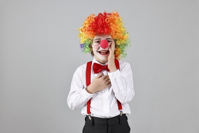 Happy little boy in clown wig and red nose on grey background. Surprise party