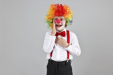 Photo of Happy little boy in clown wig and red nose on grey background. Surprise party