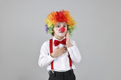 Photo of Cute little boy in clown wig and red nose on grey background. Surprise party