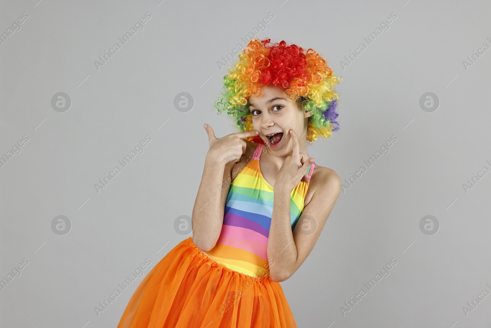 Photo of Happy girl dressed like clown on grey background. Surprise party