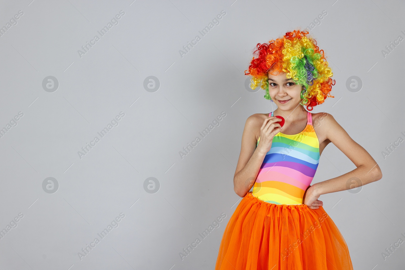 Photo of Cute girl dressed like clown on grey background, space for text. Surprise party