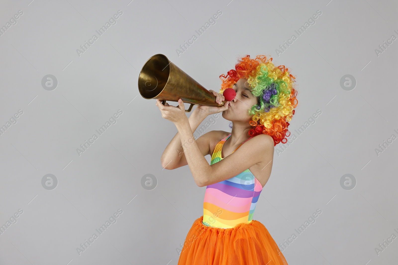 Photo of Girl dressed like clown with megaphone on grey background, space for text. Surprise party