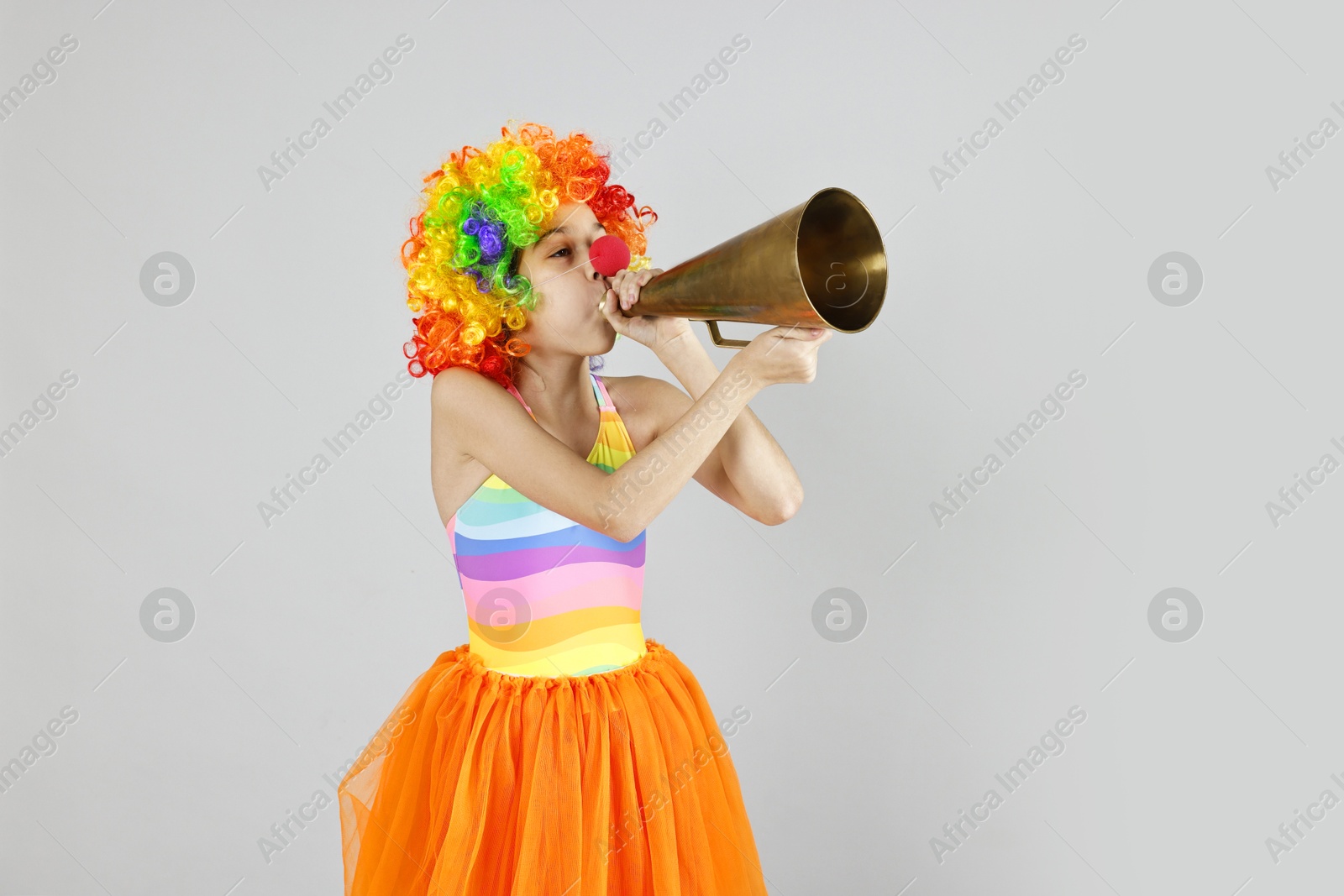 Photo of Girl dressed like clown with megaphone on grey background. Surprise party