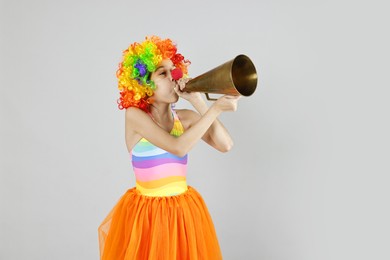 Girl dressed like clown with megaphone on grey background. Surprise party