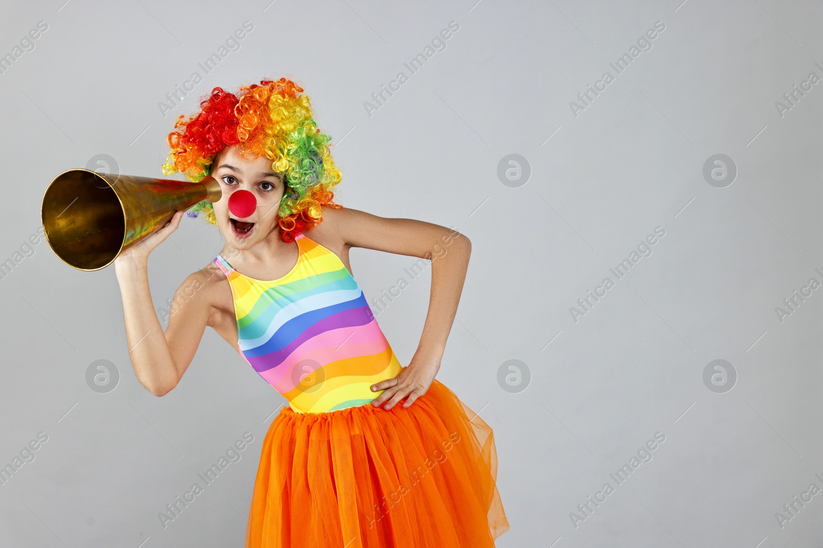 Photo of Girl dressed like clown with megaphone on grey background, space for text. Surprise party