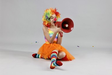 Girl dressed like clown shouting in megaphone on grey background. Surprise party