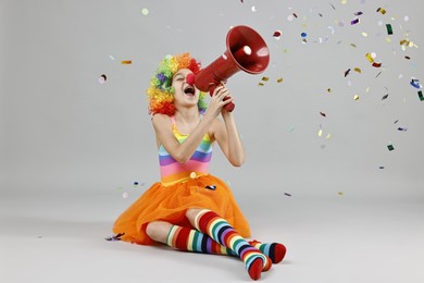 Photo of Girl dressed like clown shouting in megaphone under flying confetti on grey background. Surprise party