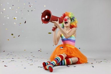 Photo of Girl dressed like clown shouting in megaphone under flying confetti on grey background, space for text. Surprise party