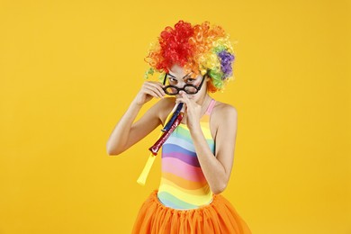 Photo of Girl dressed like clown with blowers on yellow background. Surprise party