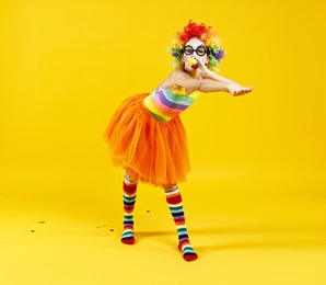 Photo of Girl dressed like clown with blowers on yellow background. Surprise party