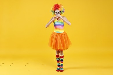 Photo of Girl dressed like clown with blowers on yellow background. Surprise party