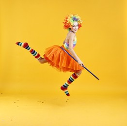 Photo of Girl dressed like clown jumping with hula hoop on yellow background. Surprise party