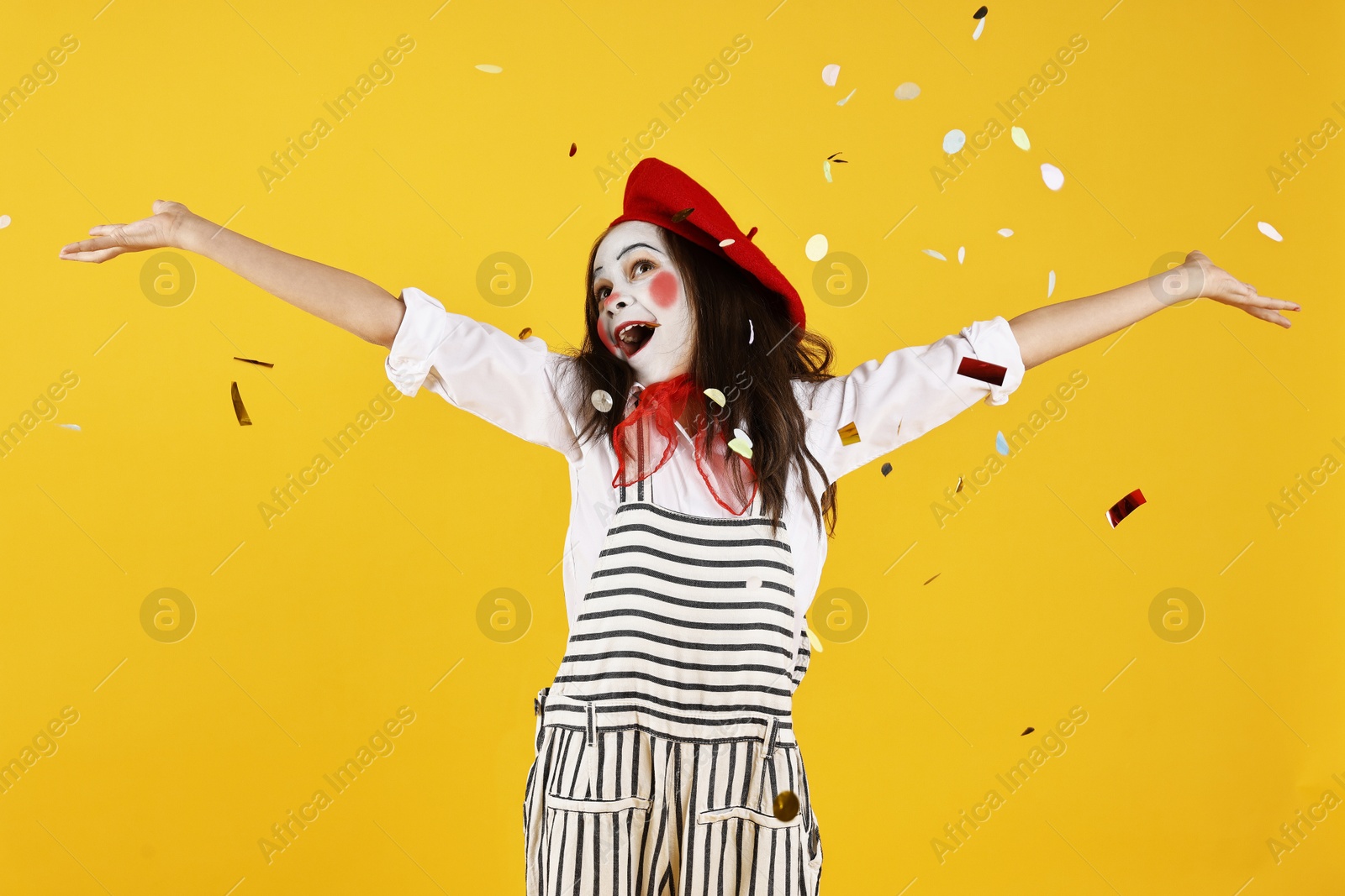 Photo of Happy girl dressed like mime under falling confetti on yellow background. Surprise party