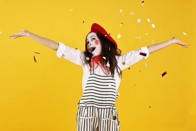 Photo of Happy girl dressed like mime under falling confetti on yellow background. Surprise party