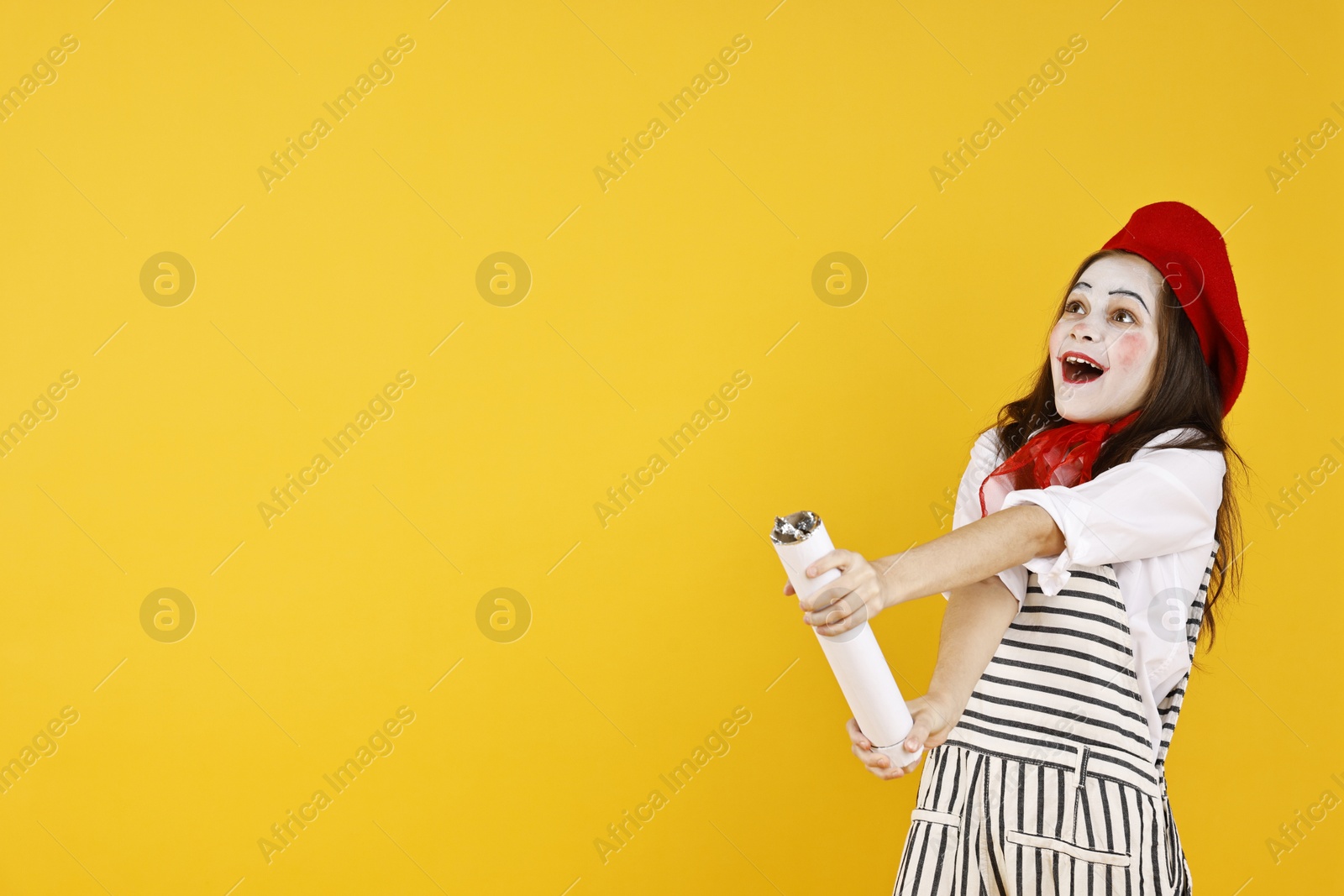 Photo of Happy girl dressed like mime with confetti popper on yellow background, space for text. Surprise party