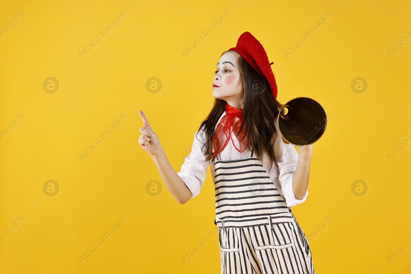 Photo of Cute girl dressed like mime with megaphone pointing at something on yellow background, space for text. Surprise party