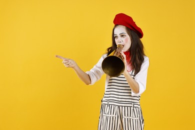 Photo of Cute girl dressed like mime with megaphone pointing at something on yellow background, space for text. Surprise party