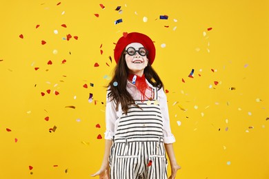 Photo of Happy girl dressed like mime under falling confetti on yellow background. Surprise party