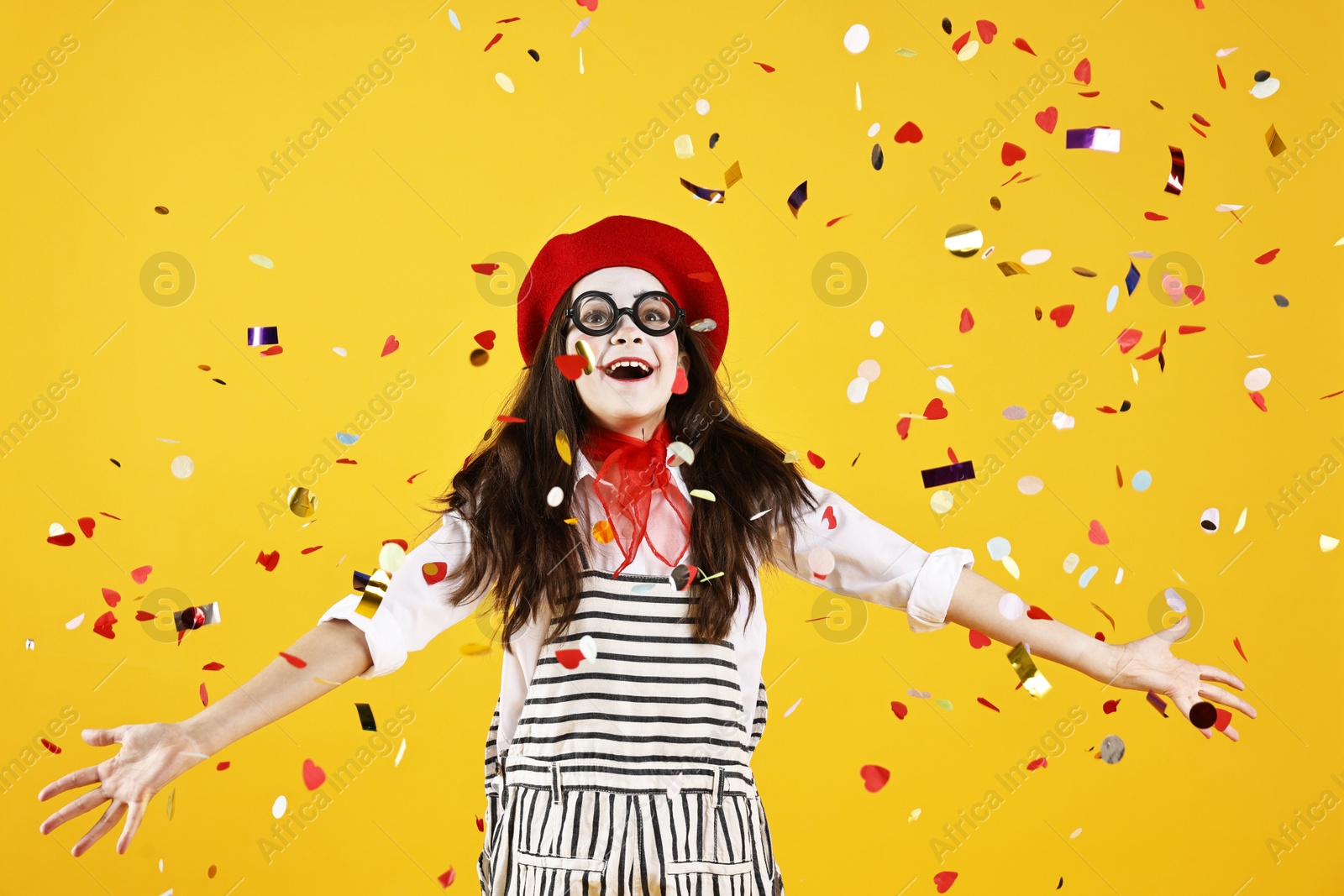 Photo of Happy girl dressed like mime under falling confetti on yellow background. Surprise party