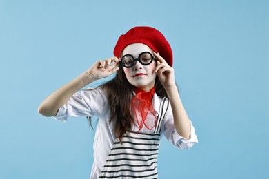 Photo of Cute girl dressed like mime on light blue background. Surprise party